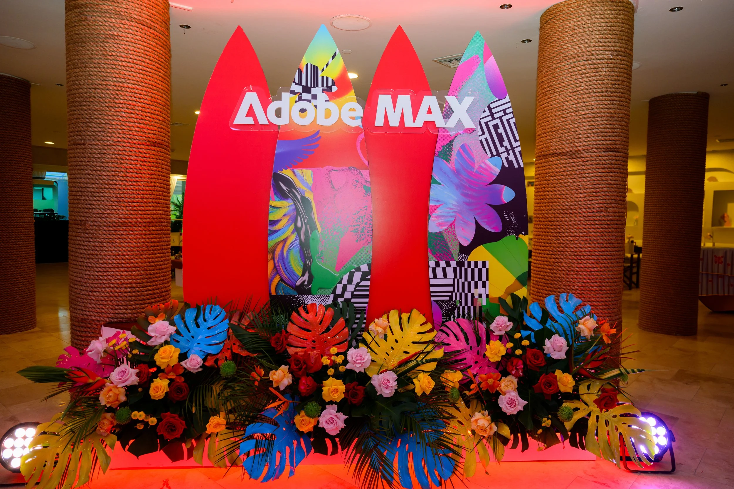 Adobe MAX lobby with surfboard-shaped red signage and a tropical floral floor piece