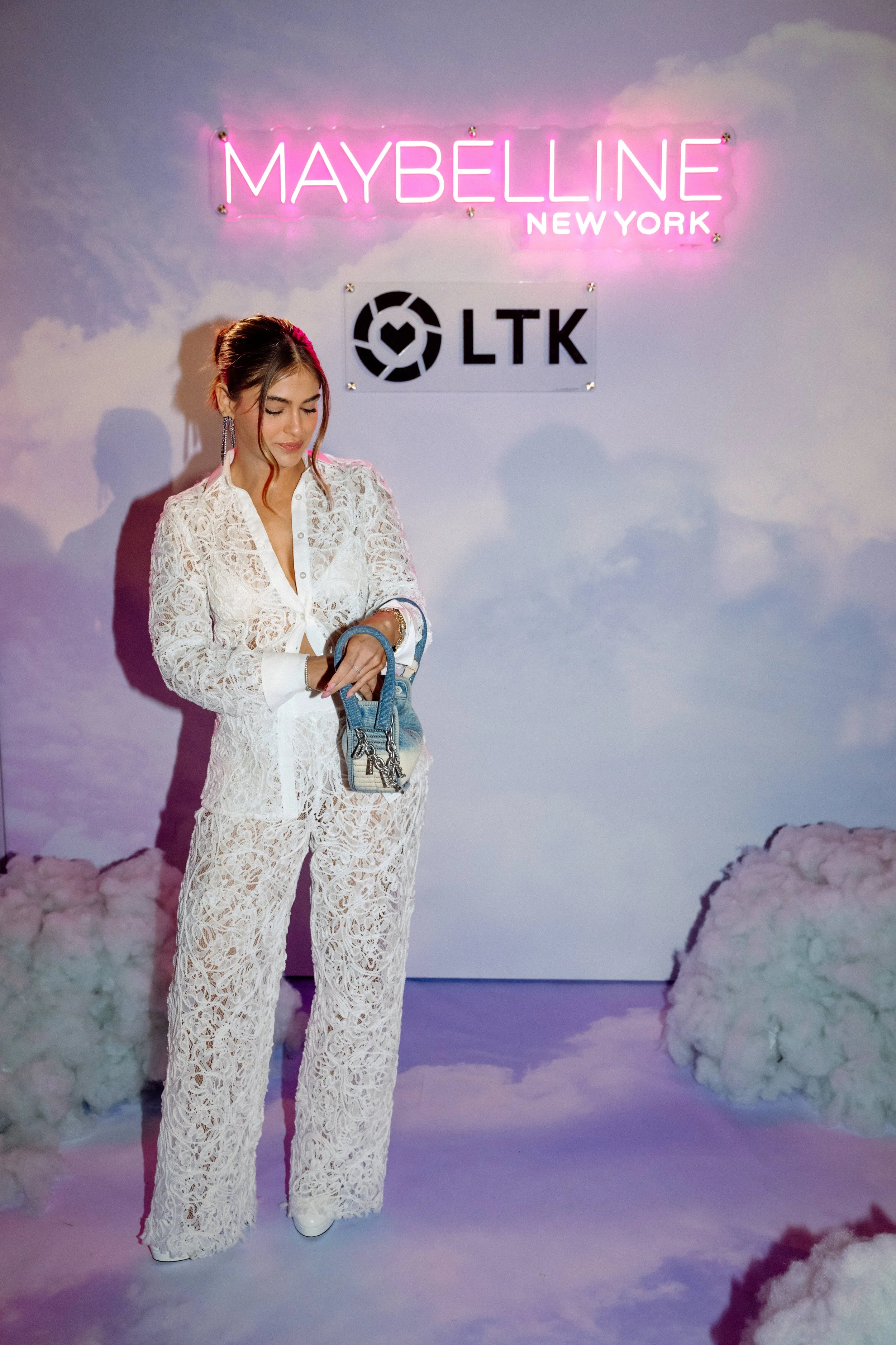 Guest in white lace in front of the cloud-themed Maybelline and LTK backdrop at night