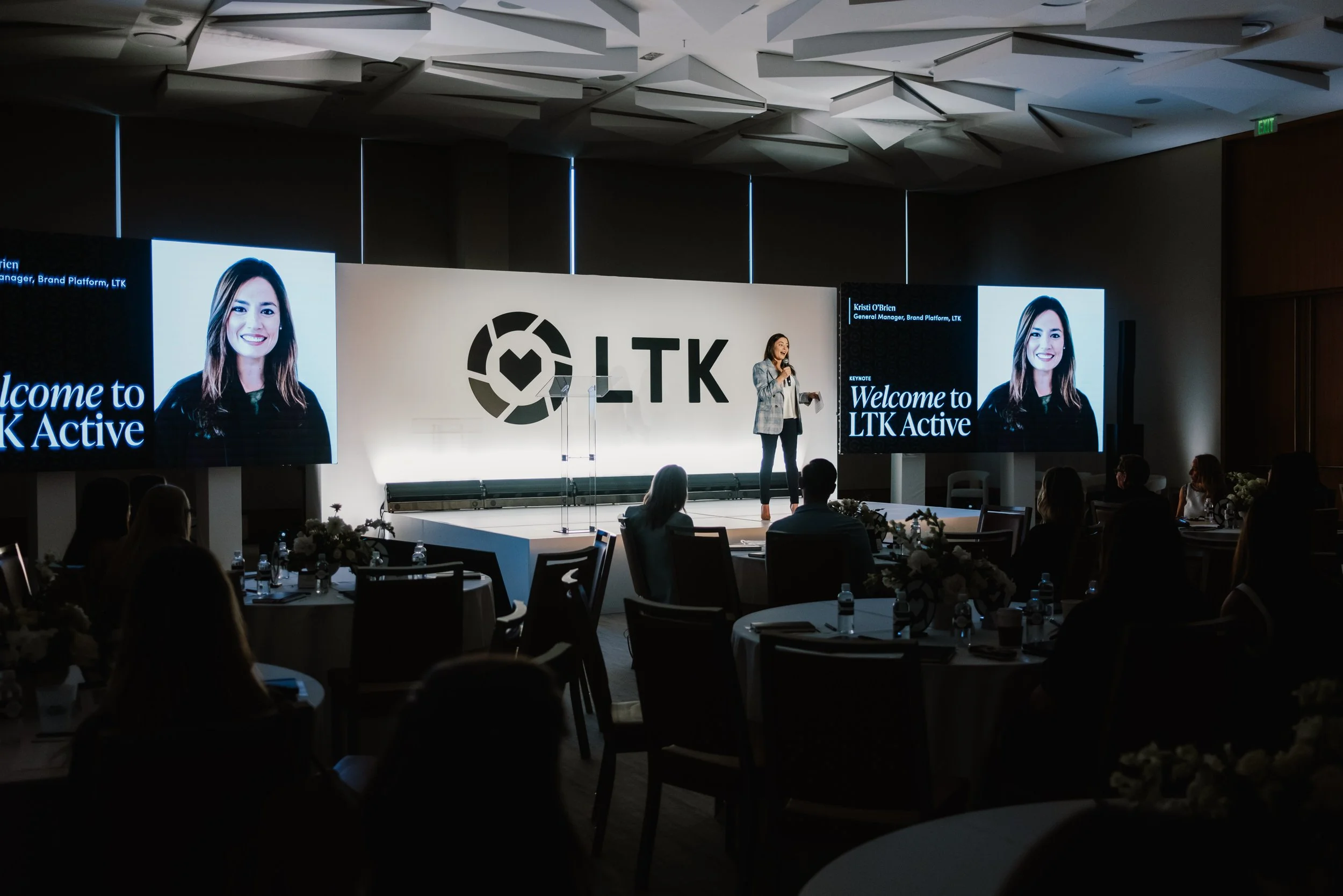 Keynote presentation in a darkened ballroom with an LTK logo backdrop and projection screens