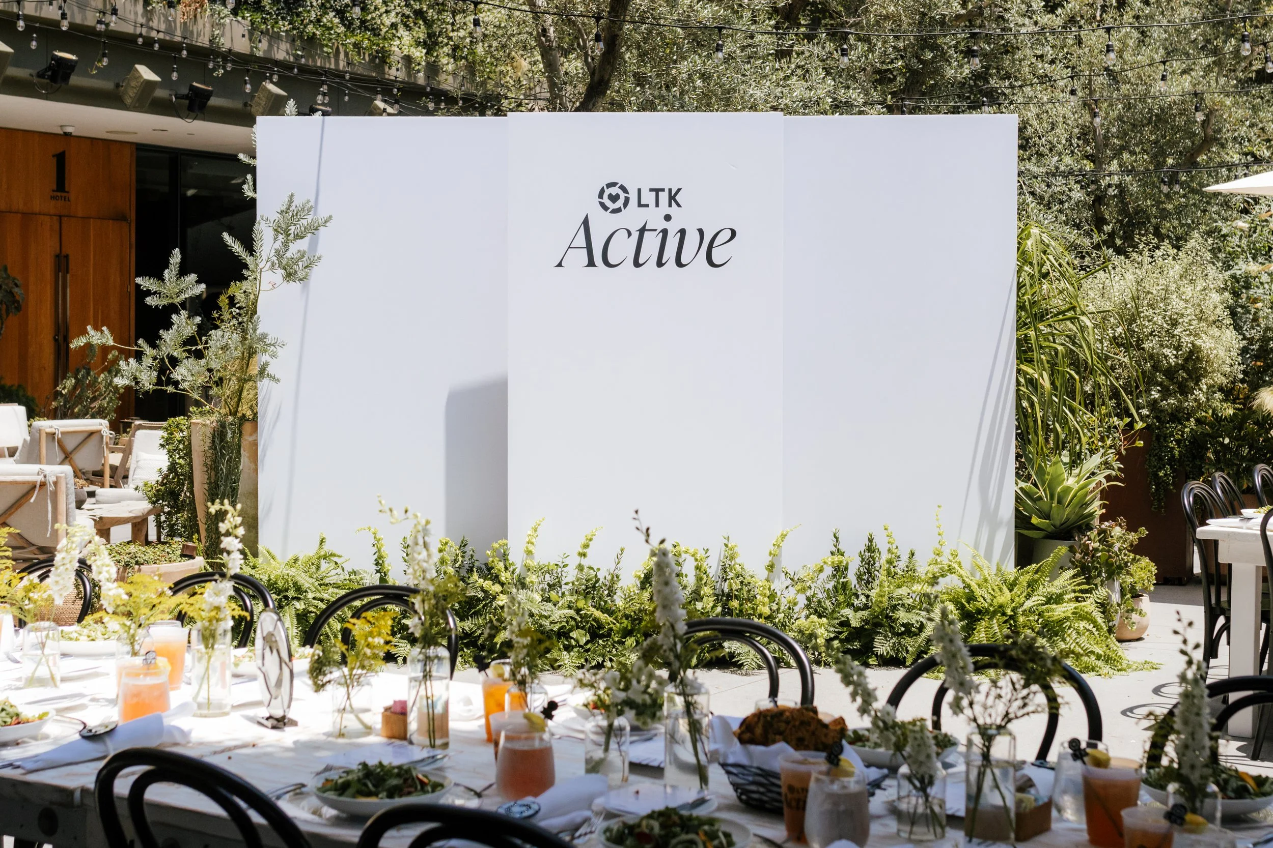 Outdoor summit dining table with floral centrepieces beside an LTK Active backdrop banner