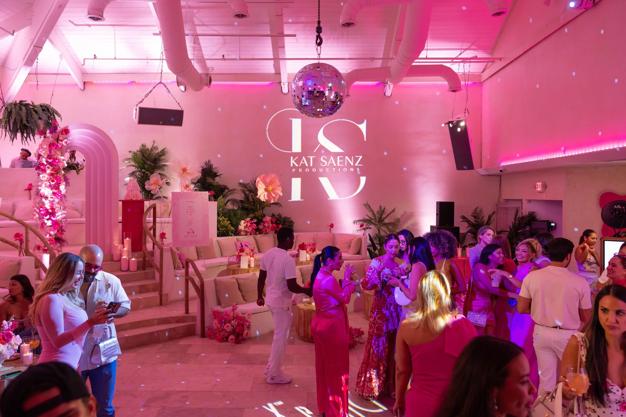 Crowd socialising under a disco ball with the KSP monogram projected in pink light