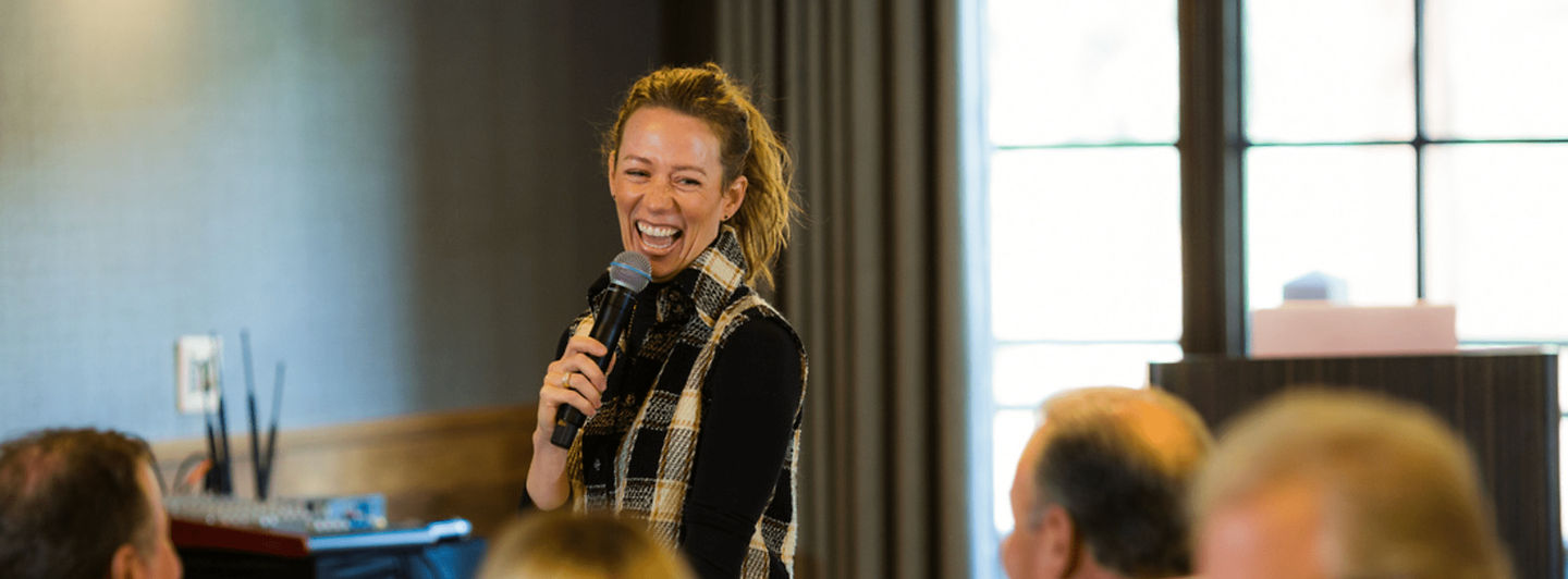 Kelsey laughing on stage with a microphone