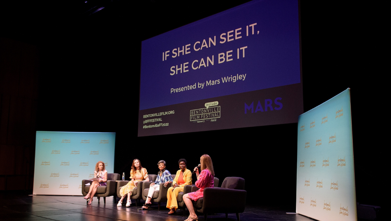 Five panelists on stage at Bentonville Film Festival in front of an “If she can see it, she can be it” screen