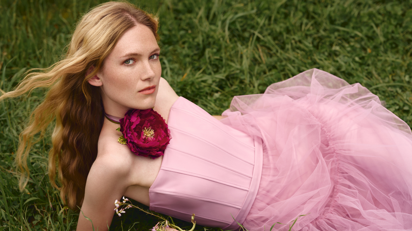 Woman in a pink tulle gown lying in grass with a floral corsage — Helena Simon campaign