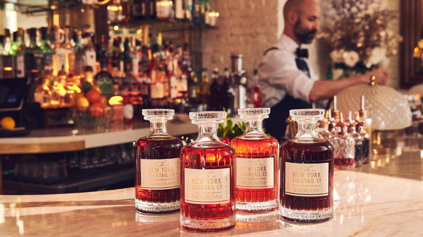 Four negroni decanters on a marble bar with a bartender behind — New York Cocktail Co.