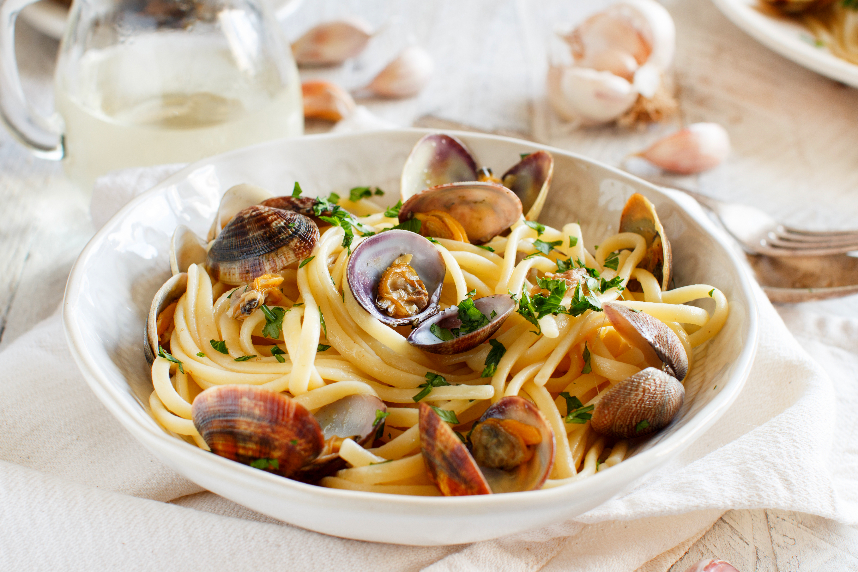 Bowl of spaghetti alle vongole with clams and parsley, white wine and garlic behind