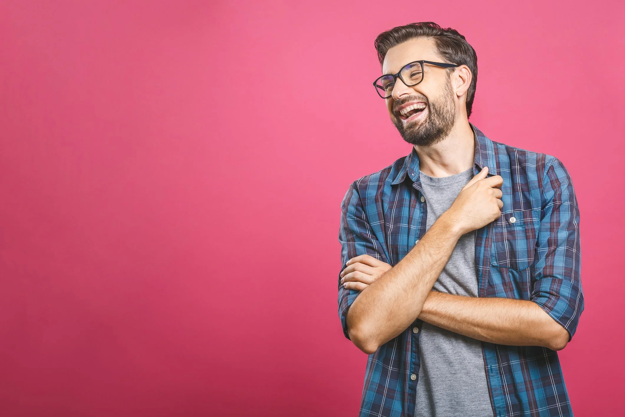 Bearded man with glasses laughing against a pink background