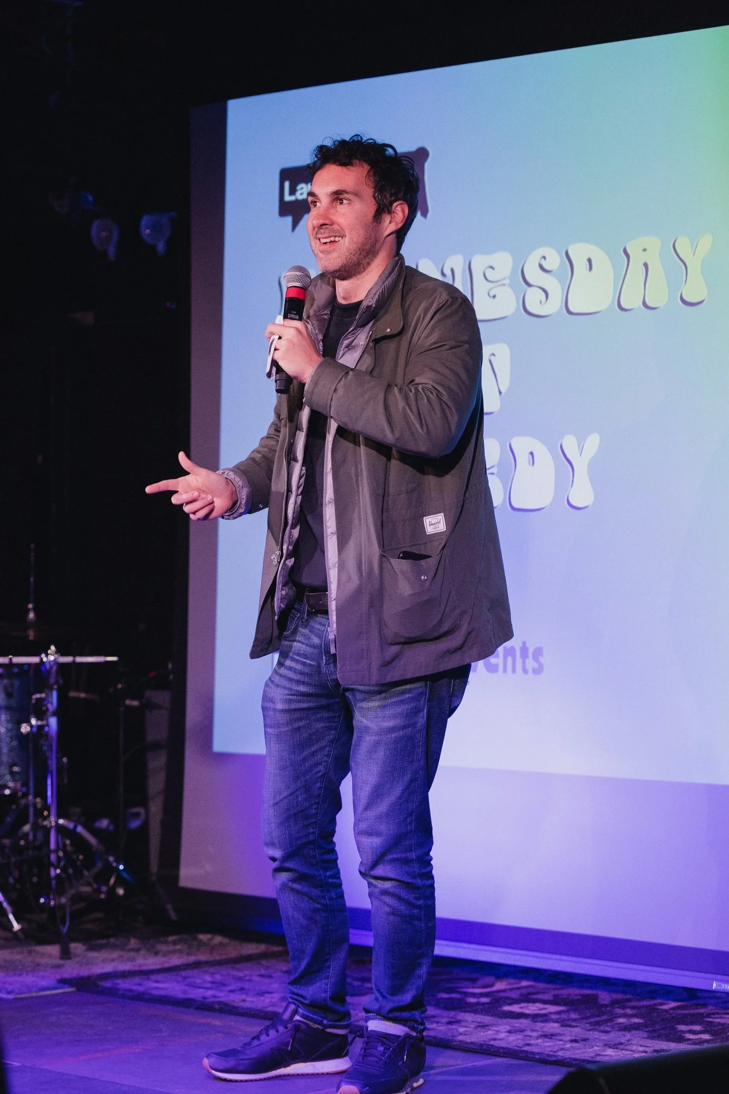 Male stand-up comedian on stage in front of a Laugh.Events branded screen