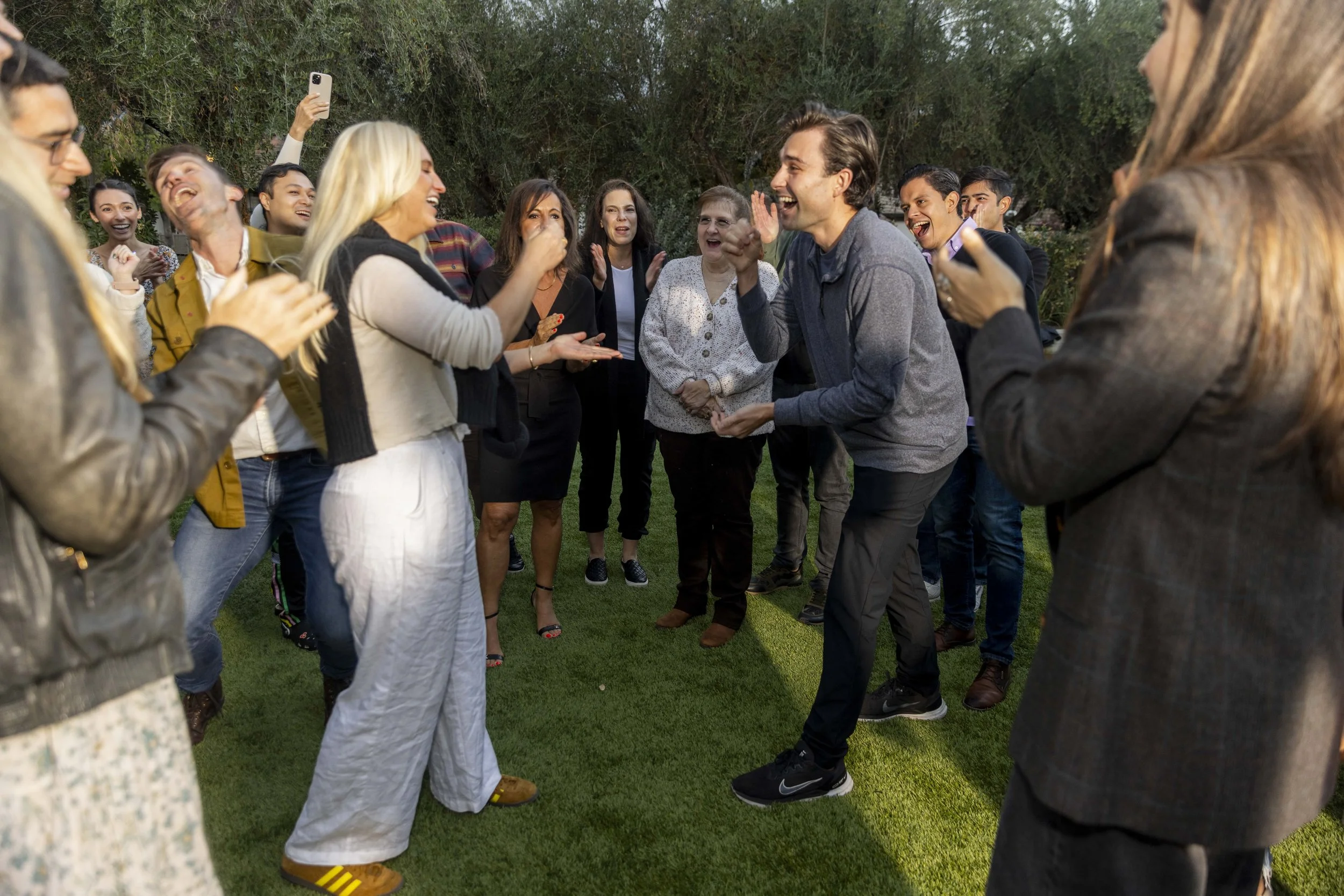 Corporate employees laughing and clapping in a circle outdoors during a team-building session