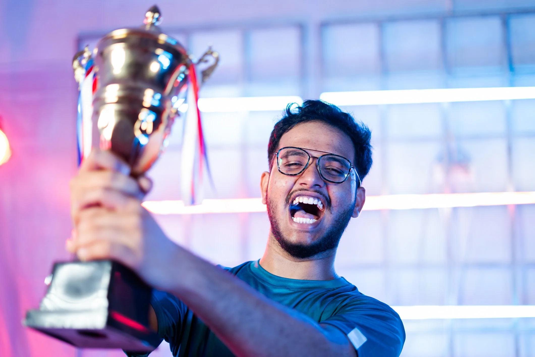 Man cheering and holding a trophy aloft under neon light