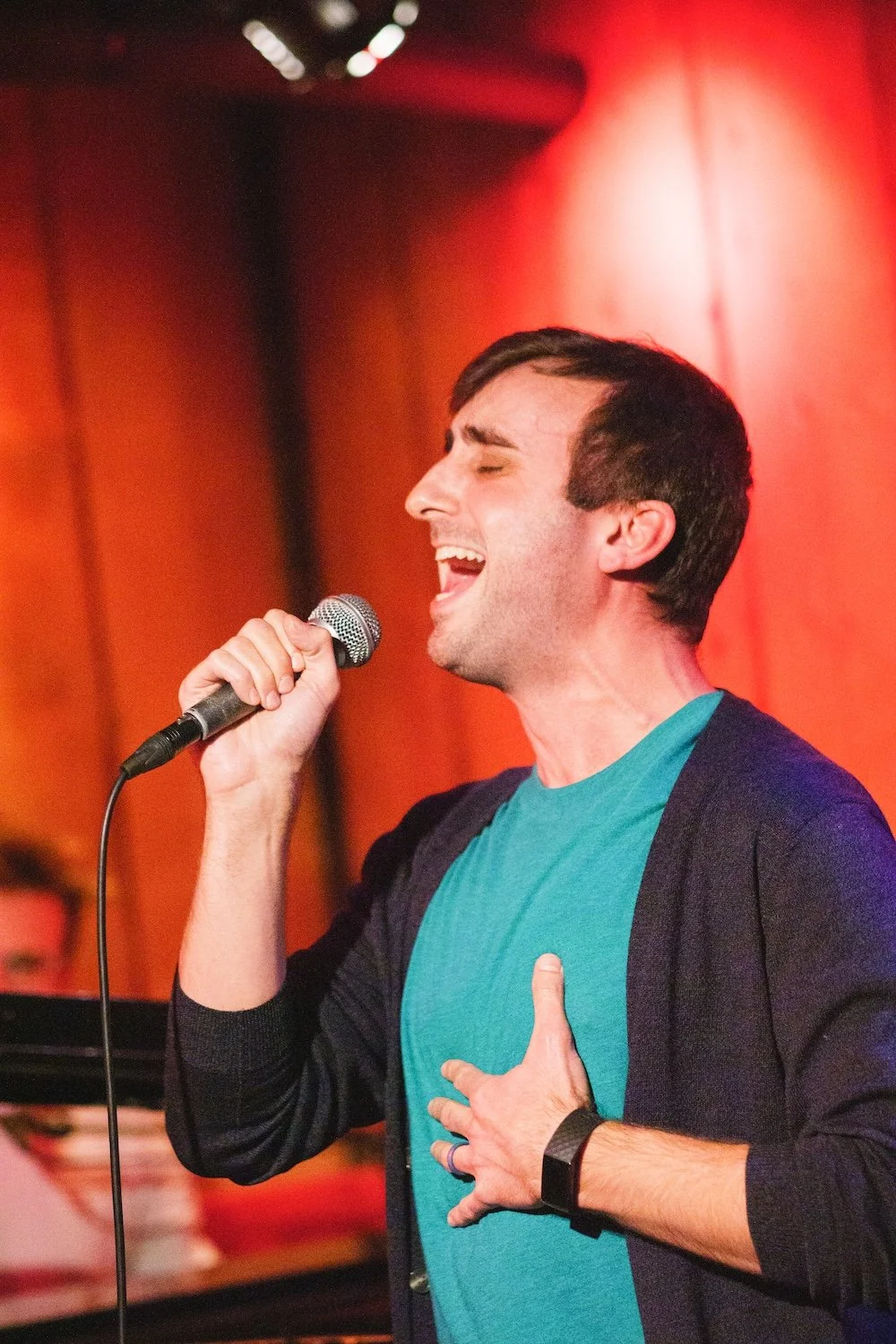 Performer singing into a microphone on a red-lit stage