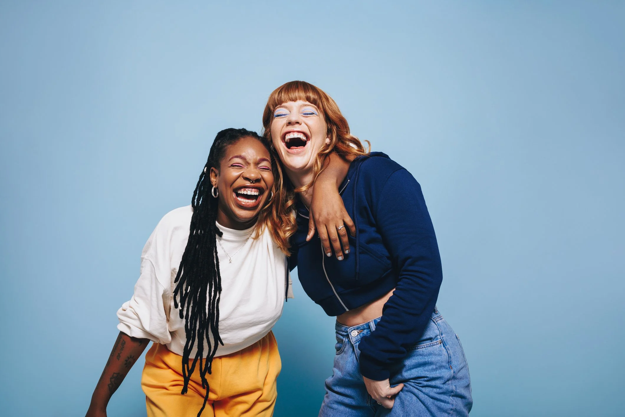 Two women laughing together against a light blue background