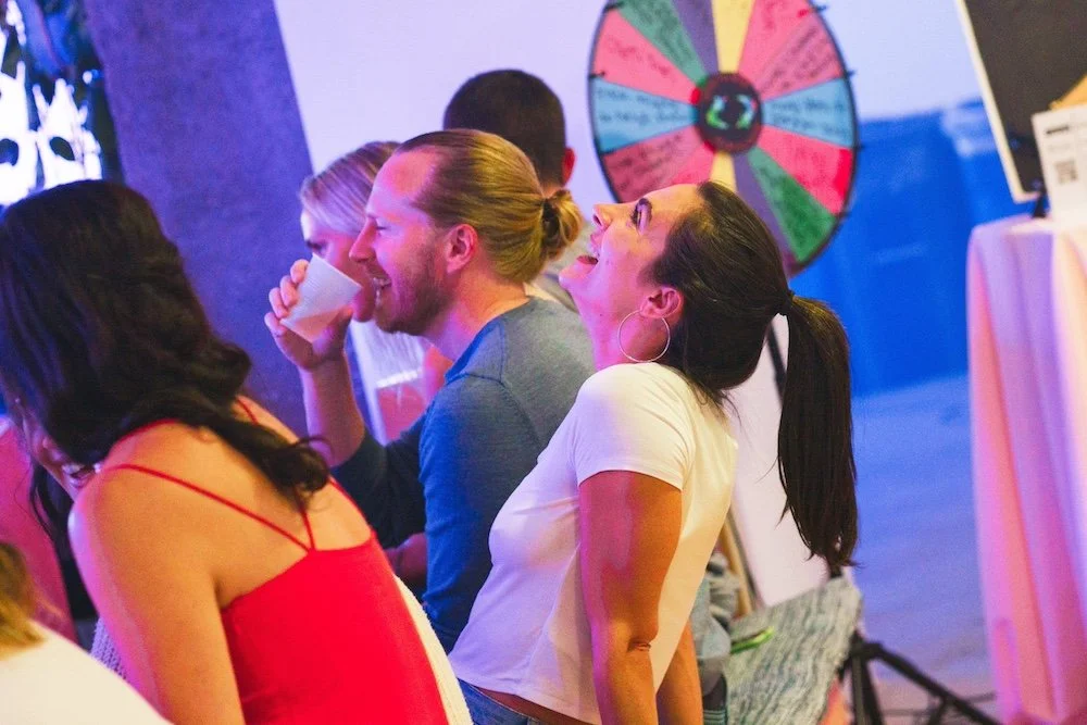 Audience members laughing at a comedy game show with a prize wheel behind them