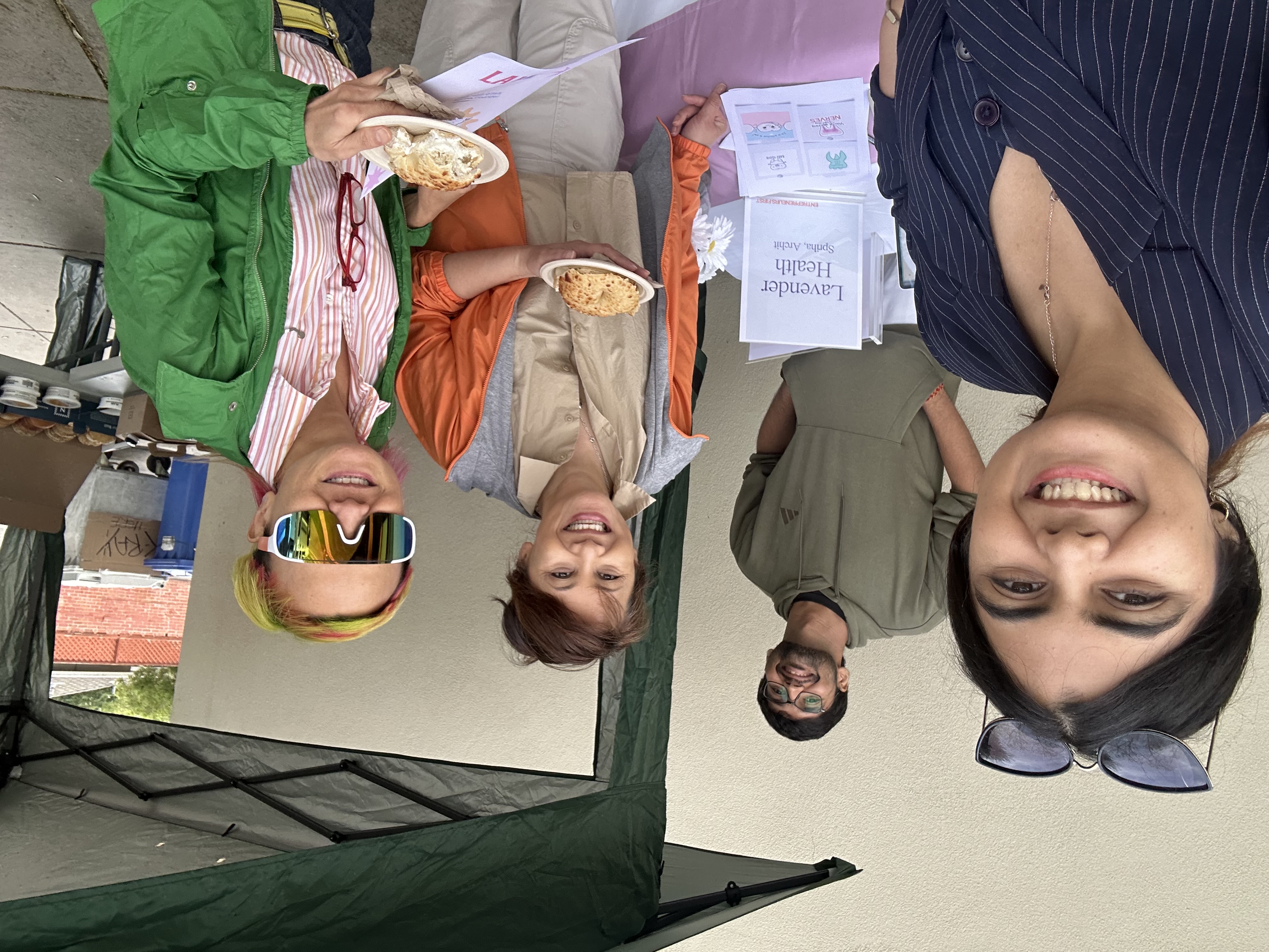 Four people smiling at a Lavender Health outdoor booth with branded materials