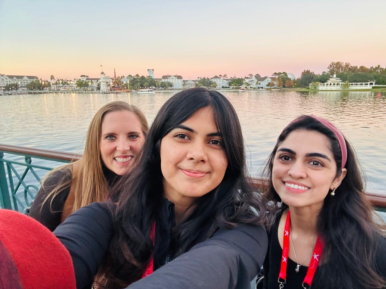 Three women in conference lanyards taking a waterfront selfie at sunset
