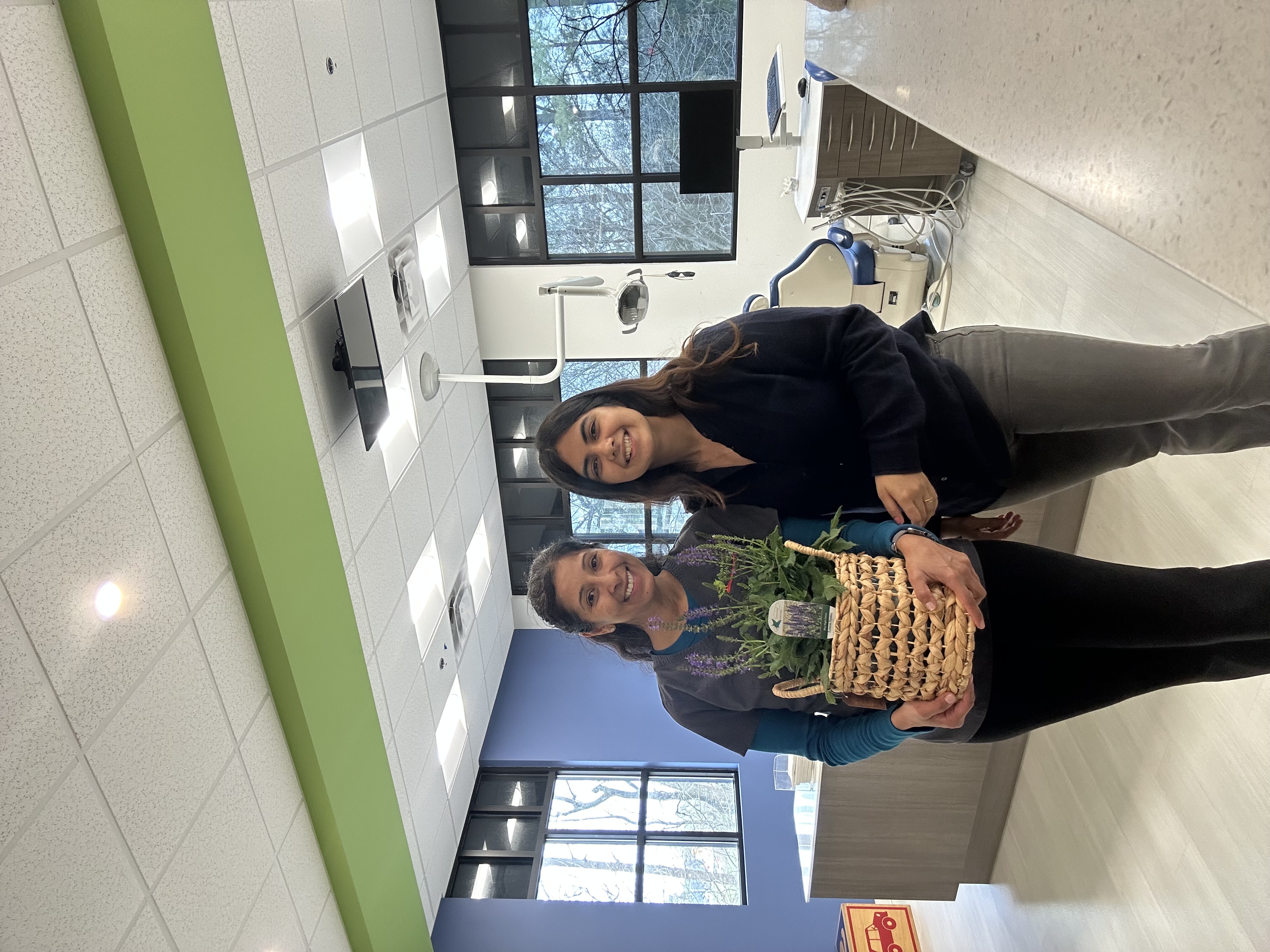 Two women smiling inside a dental practice, one holding a lavender plant basket