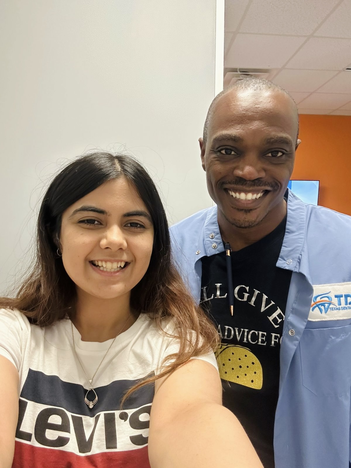A young woman and a man in dental scrubs smiling for a selfie inside a dental office
