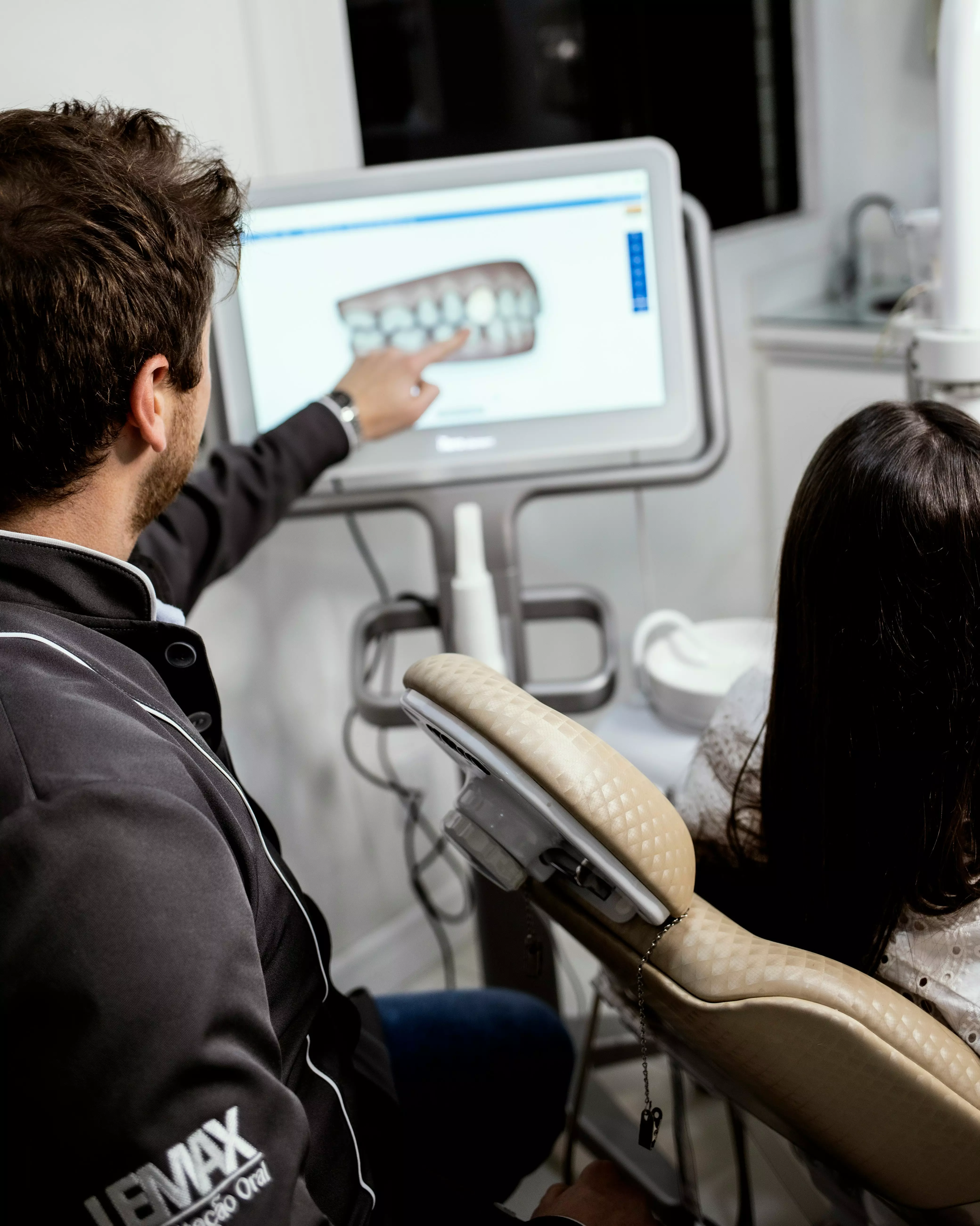 Dentist pointing at a dental X-ray on a monitor while a patient sits in the chair