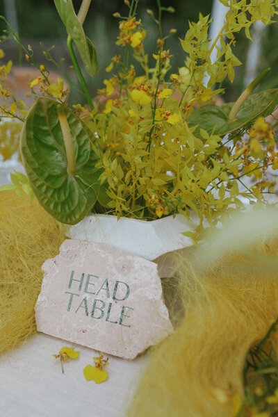 Stone Head Table signage surrounded by yellow orchids and tropical foliage