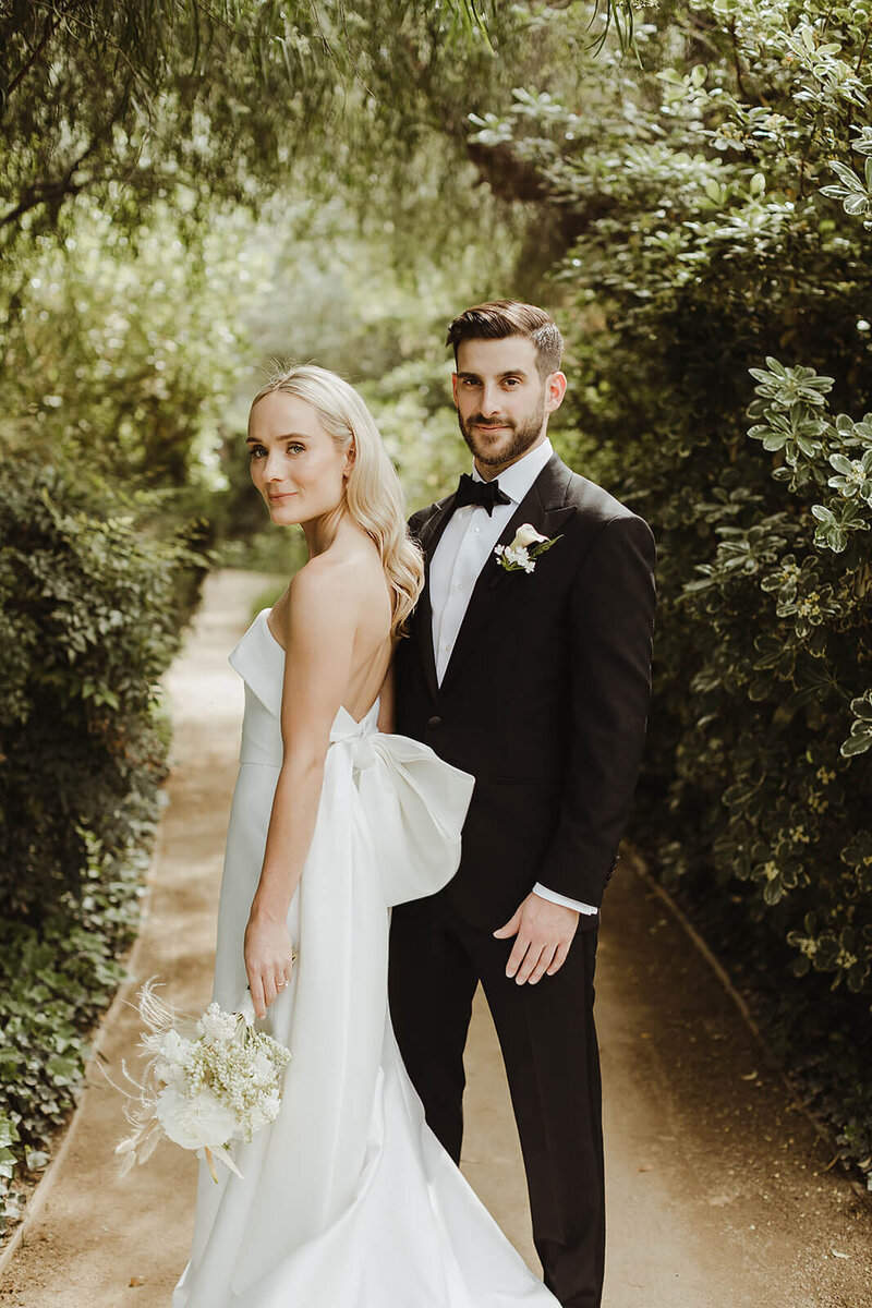 Couple on a garden path; bride in a strapless bow gown, groom in a black tux — Laura and Andrew