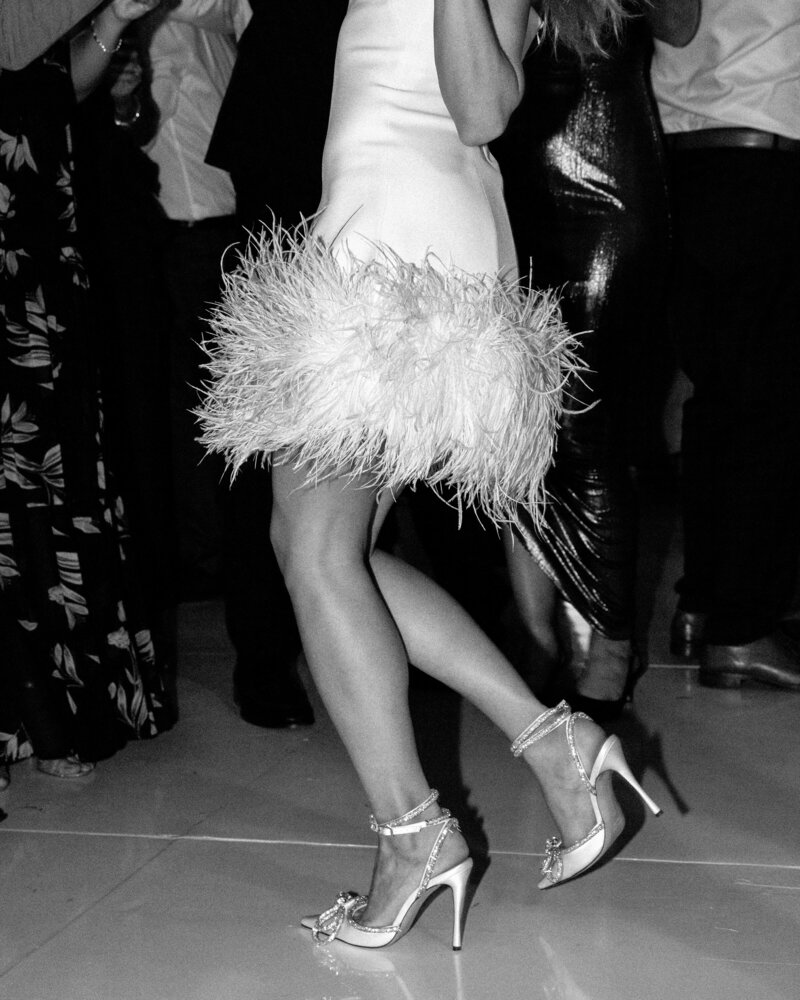Black and white photo of feather-trimmed dress and high heels dancing
