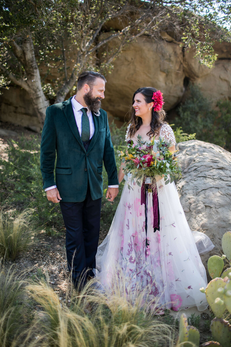 Couple in a rocky desert; bride in a floral-painted ball gown, groom in a green velvet blazer — Marisa and Mike