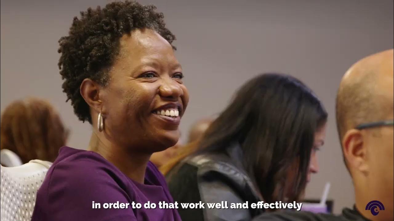 Video still — a principal smiling in the audience at a Lead Liberated convening.
