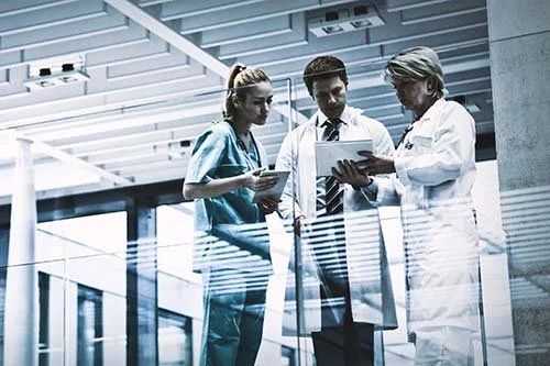 Three healthcare professionals reviewing a tablet in a hospital corridor