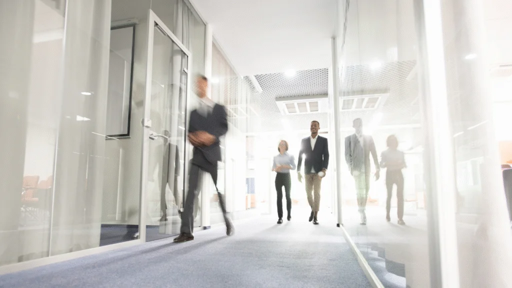 Profesionales caminando por un corredor de oficinas con paredes de vidrio