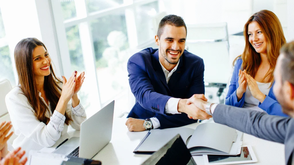 Equipo de negocios en una mesa de reunión, apretón de manos y aplausos