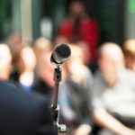 Microphone with a blurred audience, representing keynotes