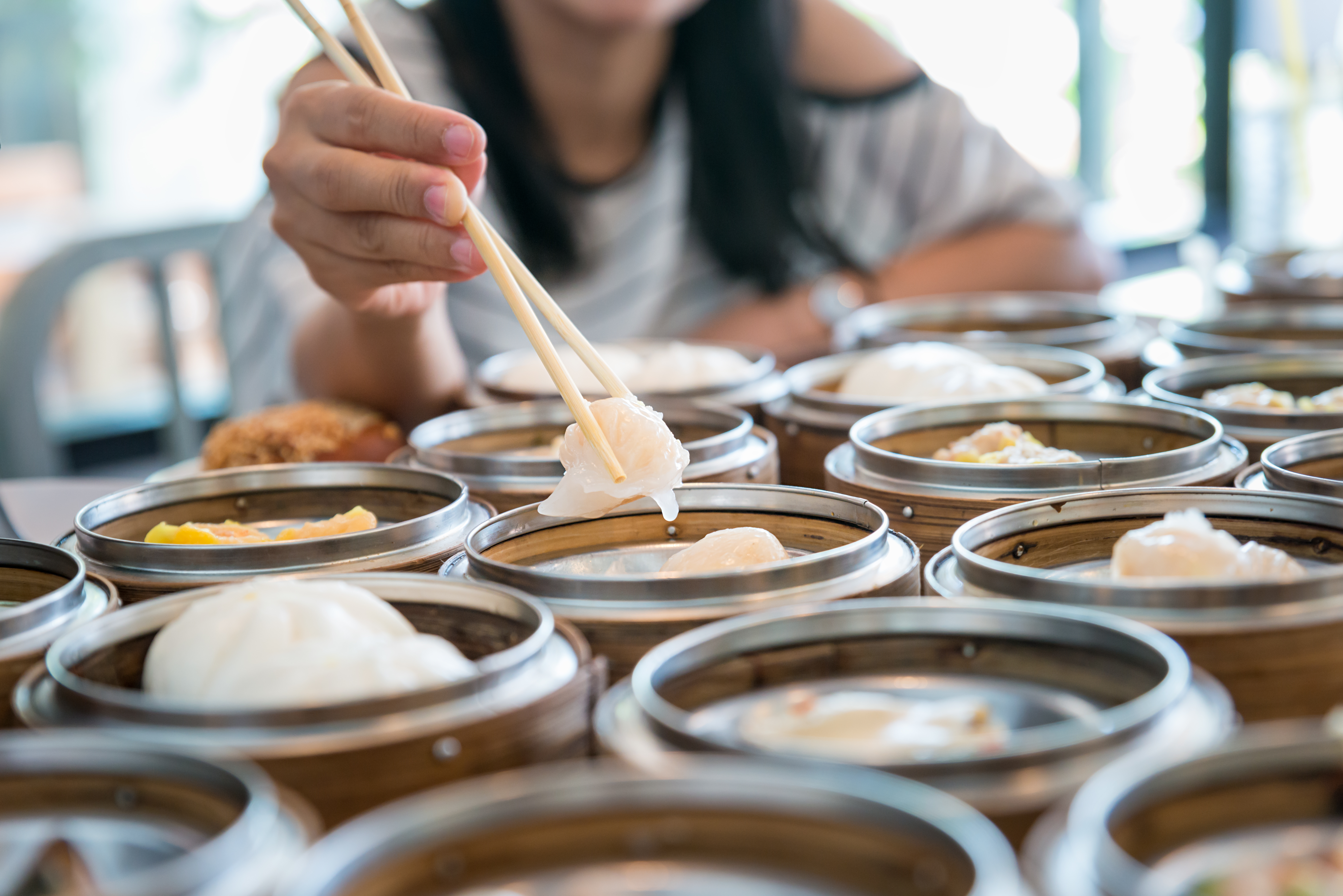 Chopsticks lifting a dumpling from bamboo steamer baskets