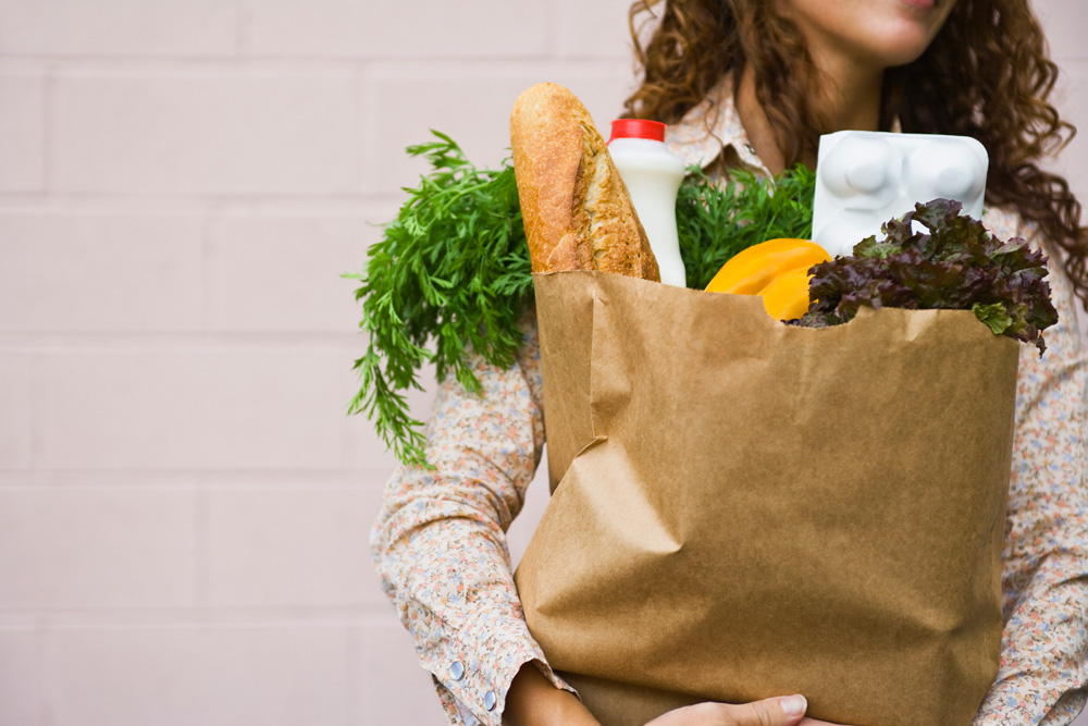 Woman holding a paper grocery bag filled with vegetables and bread
