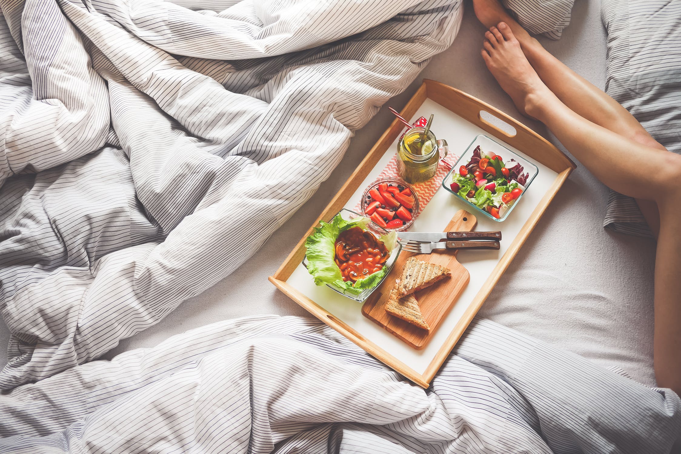 Healthy breakfast tray on a bed with salad, toast and berries