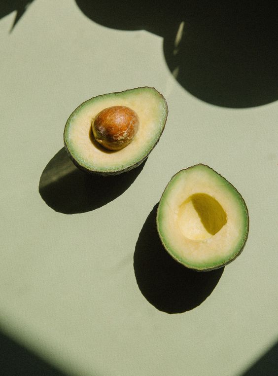 Halved avocado on a green-grey surface with leaf shadows