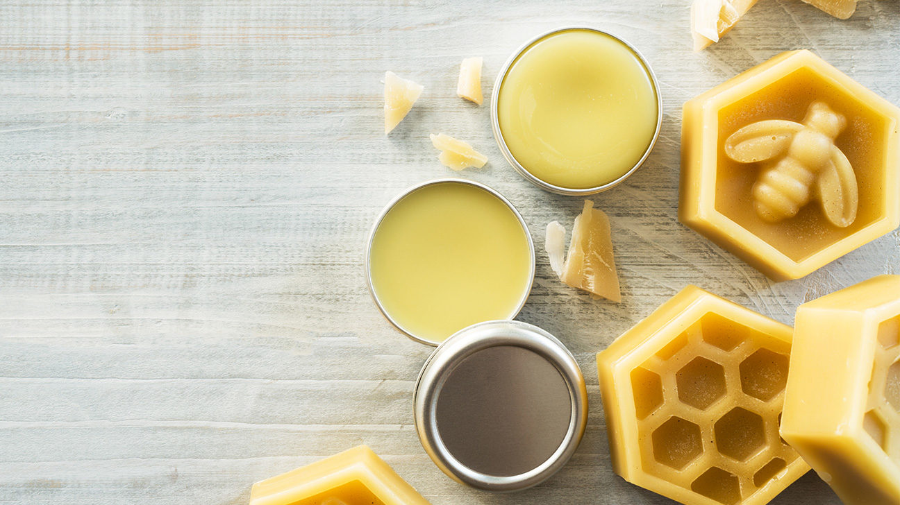 Tins of beeswax balm and hexagonal beeswax blocks on a wooden surface