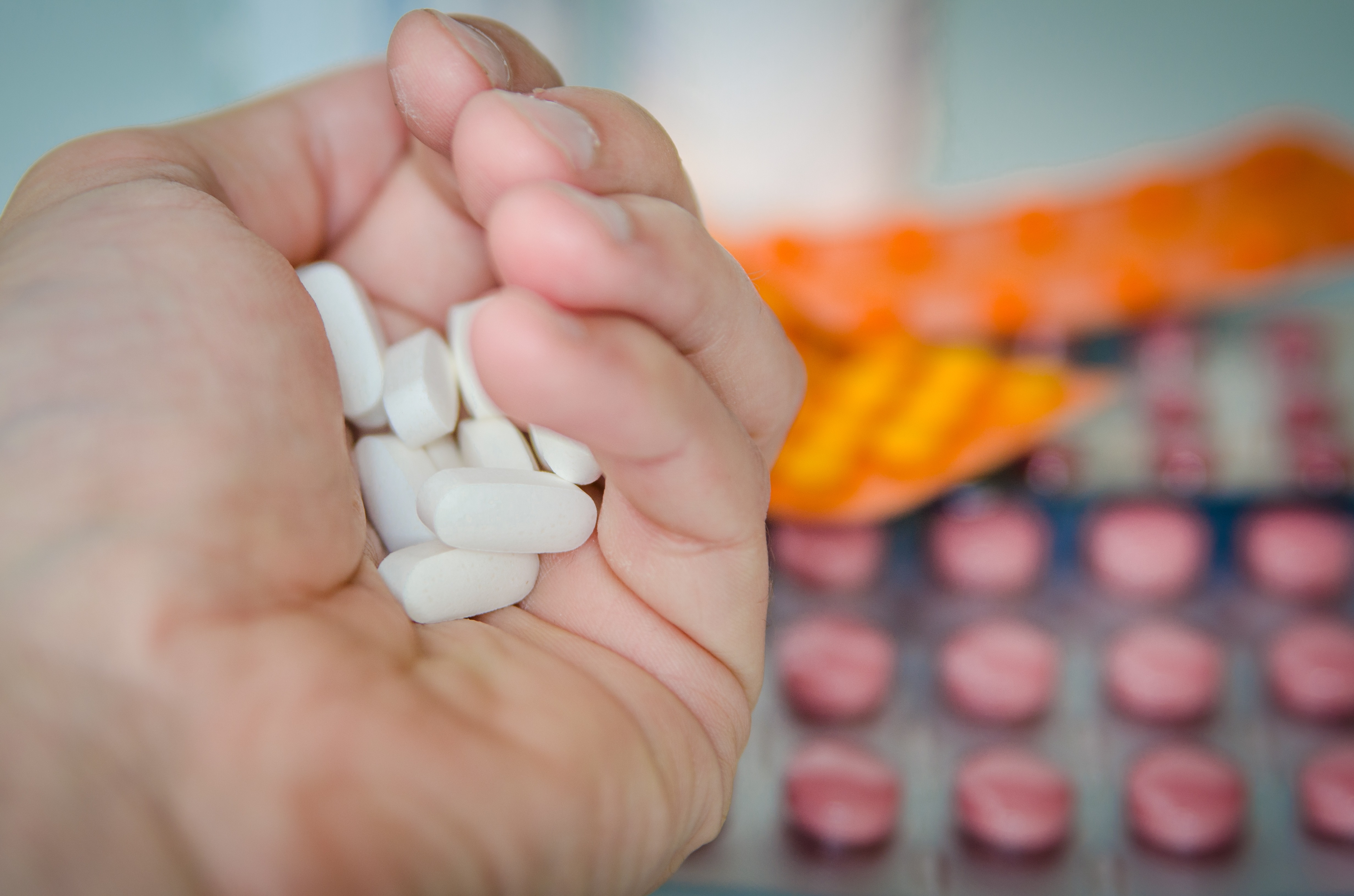 Hand holding white tablets with blister packs in the background