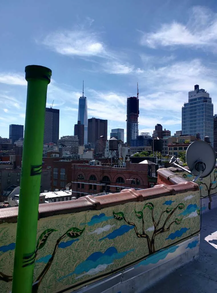 Rooftop view toward One World Trade Center with a colorful mural on the parapet wall