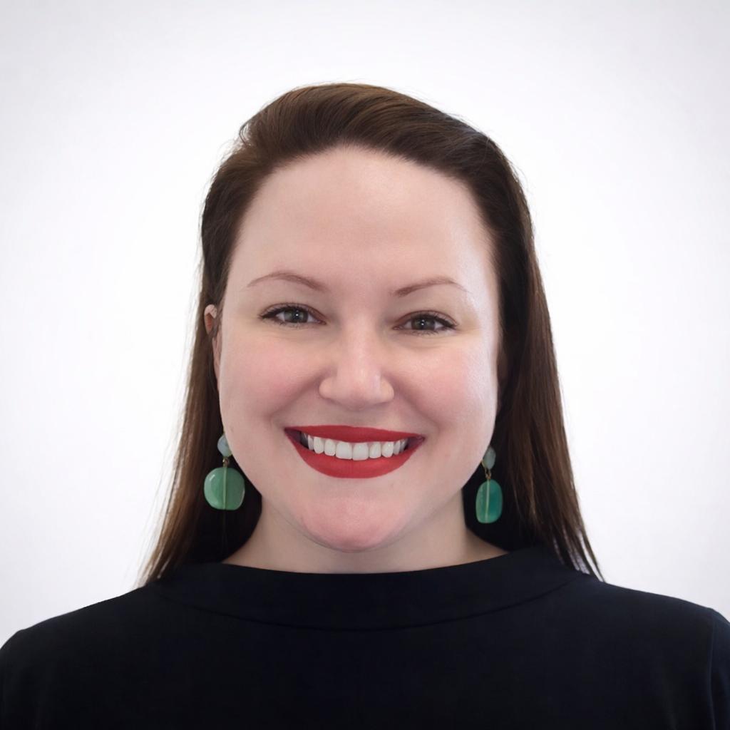 Portrait of Megan McDonough, smiling in a black top with green earrings