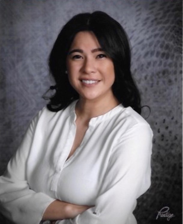 Portrait of Katherin D. Umana, smiling with arms crossed in a white blouse