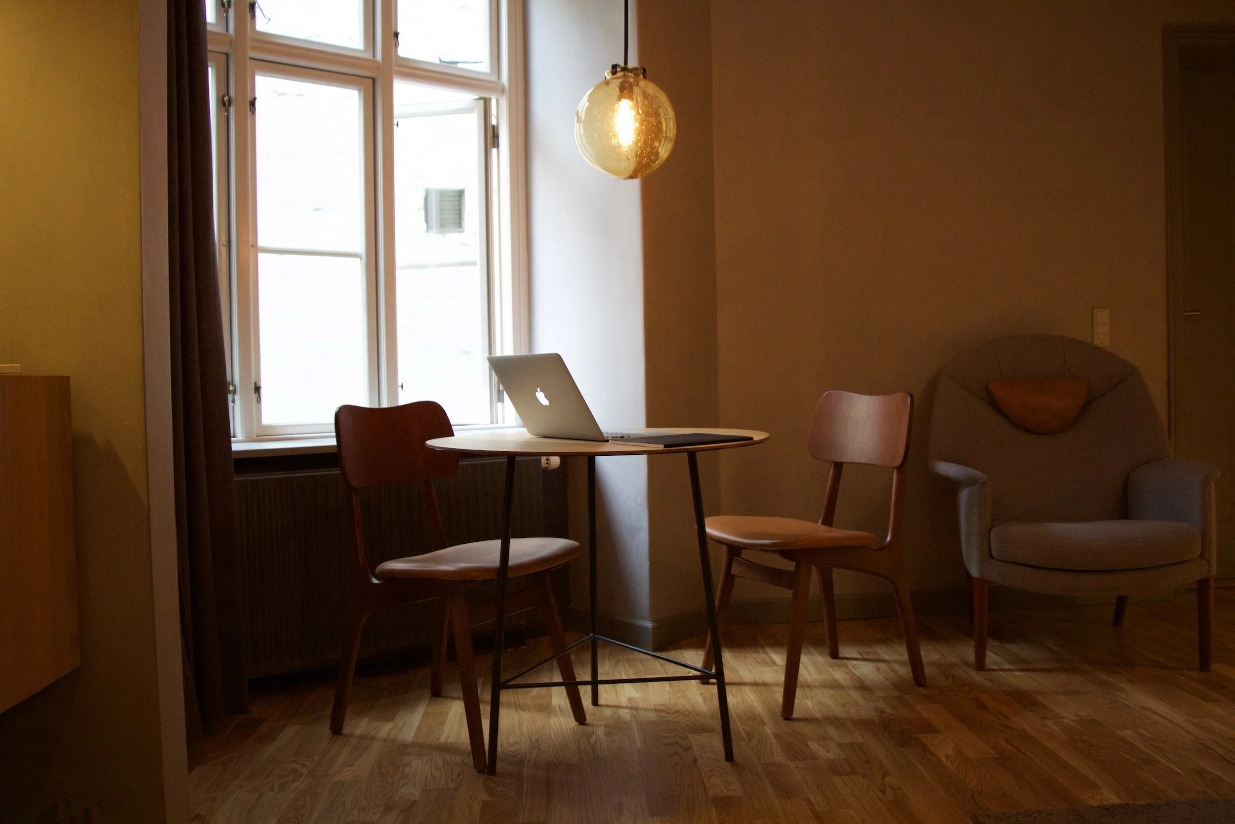 Cozy interior with a round table, laptop, two wooden chairs, a pendant globe light and a large window