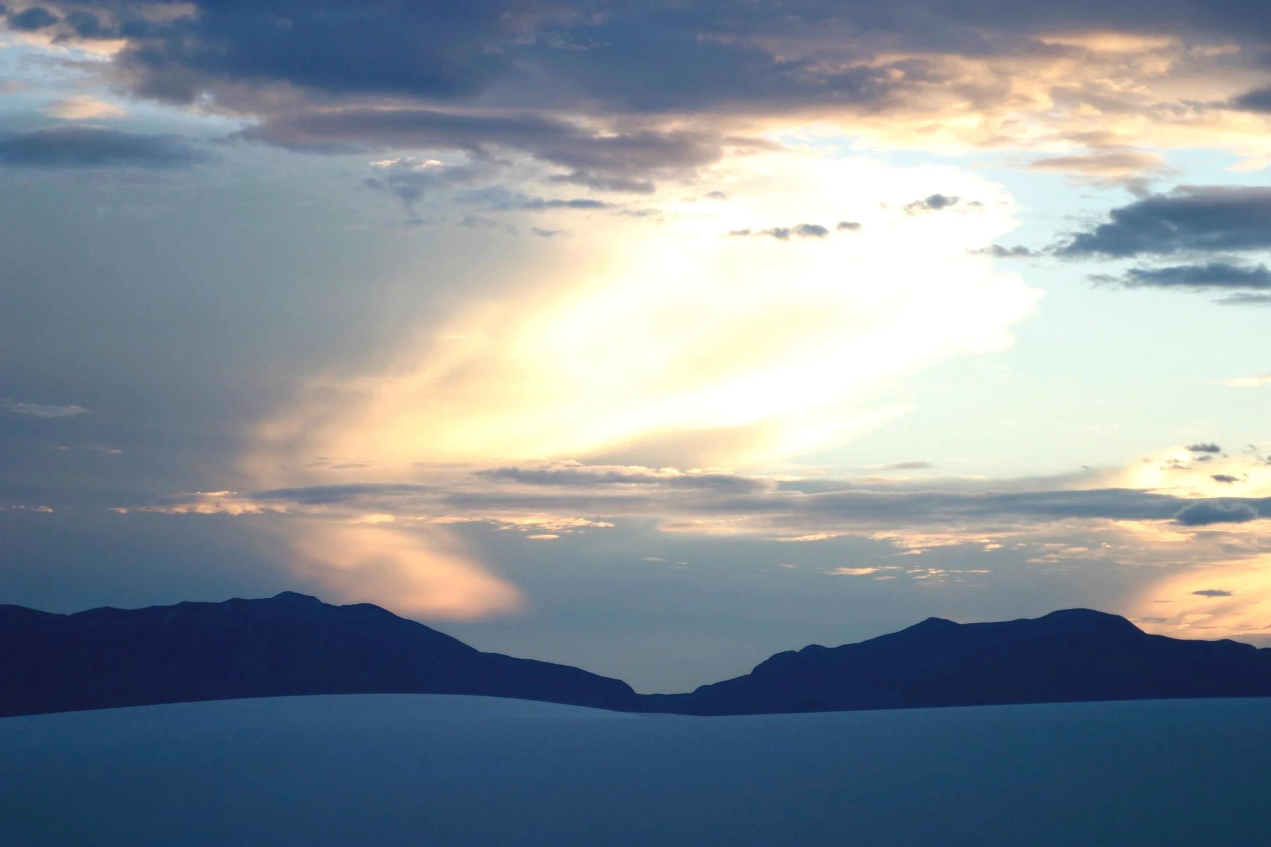Dramatic golden-hour sunset with rays of light breaking through cloud over a mountain silhouette and pale foreground
