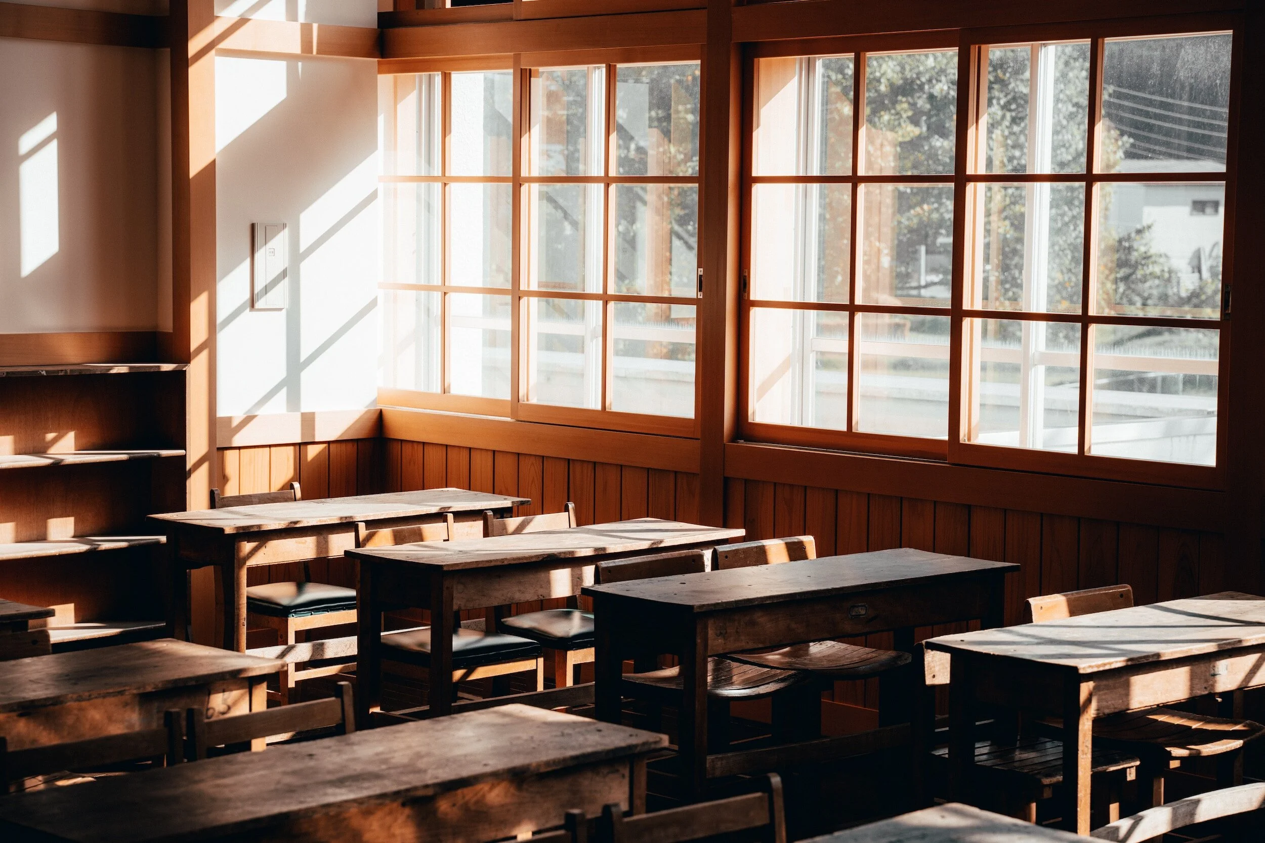 Empty sunlit classroom with rows of wooden desks and large grid windows