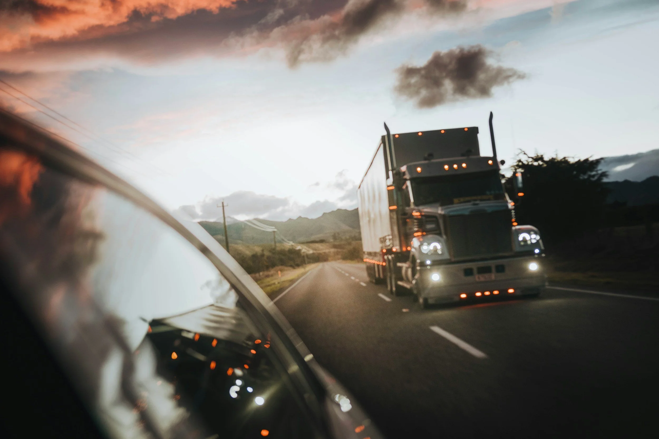 A semi-truck driving on a highway at dusk, viewed from a car window