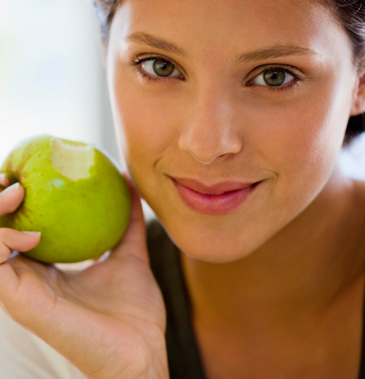 Young woman smiling while holding a bitten green apple