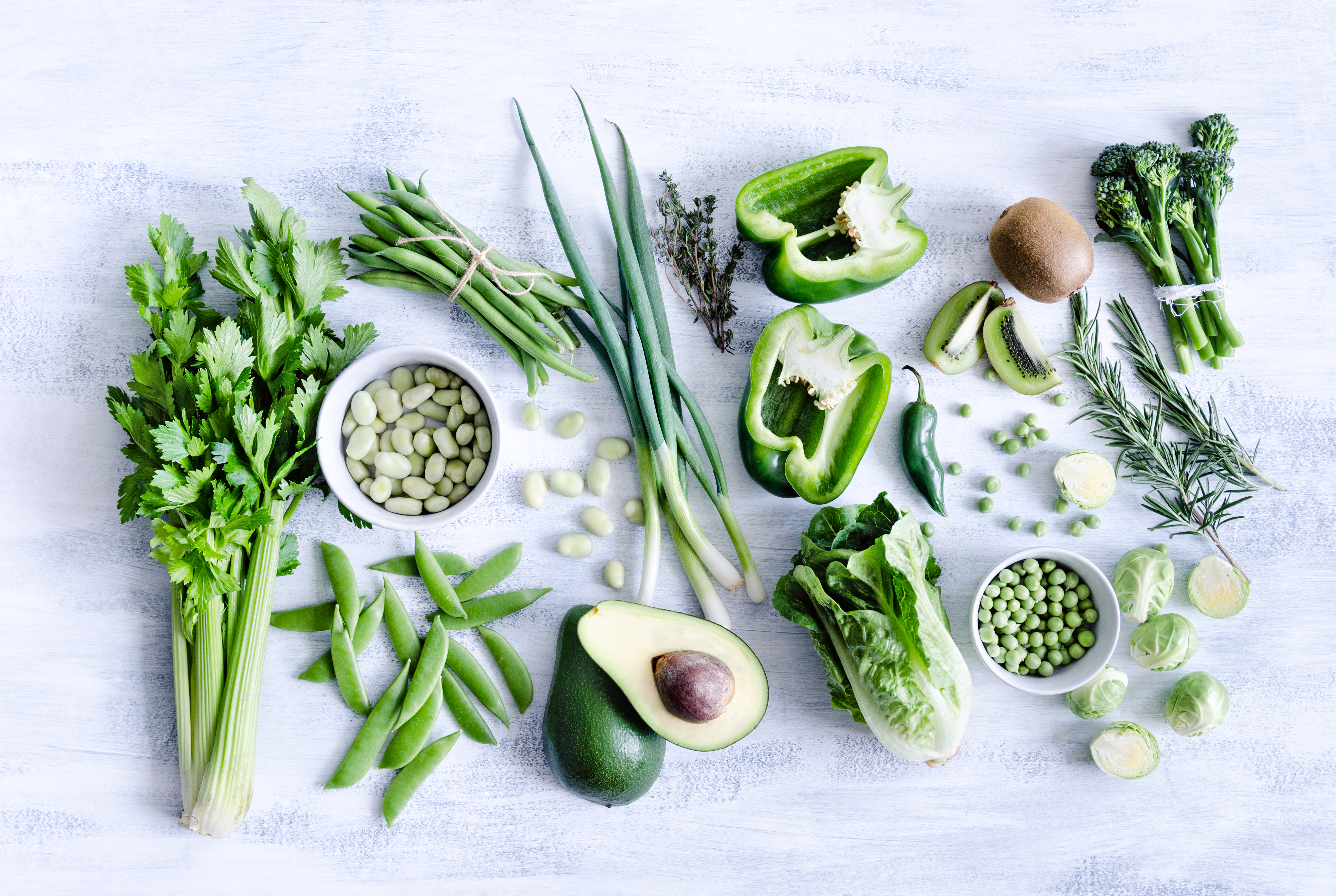 Flat-lay of assorted green vegetables on a white background