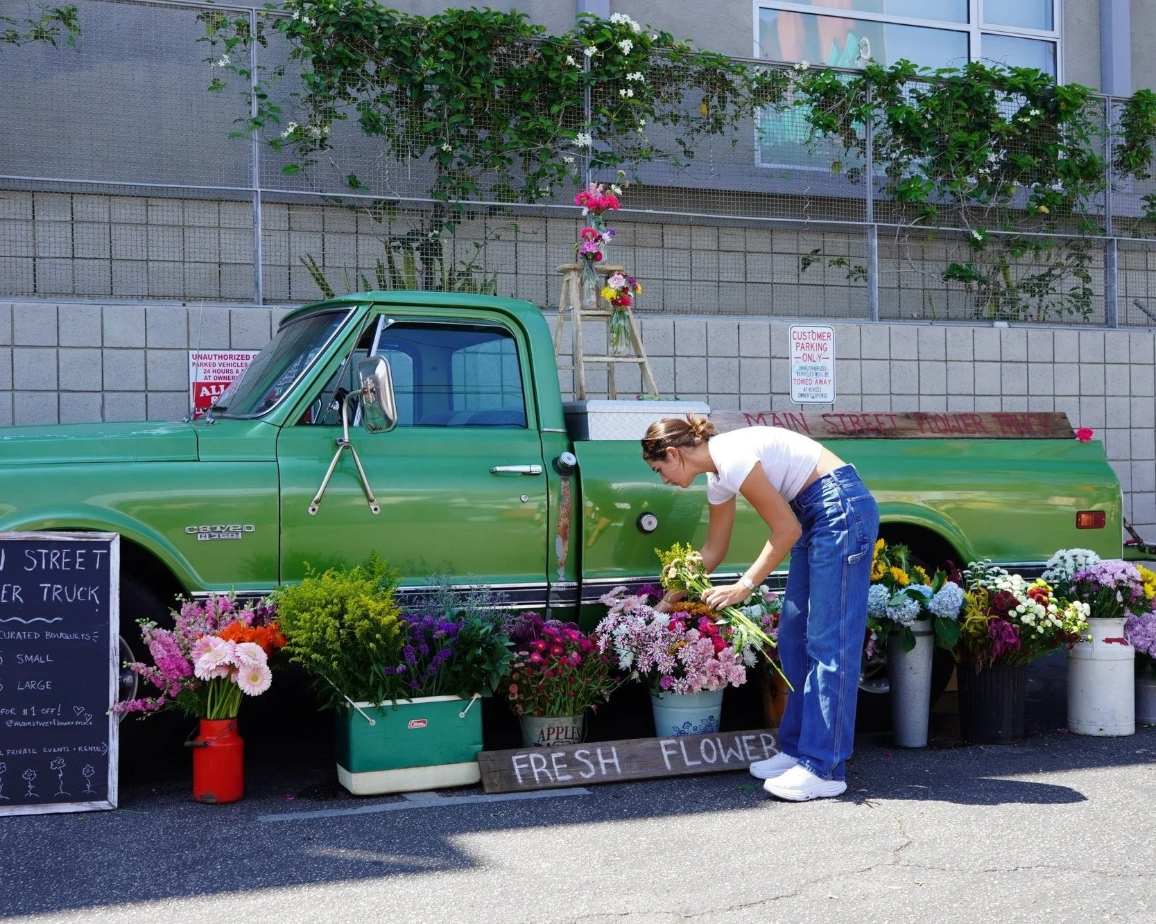 The Main Street Flower Truck parked on an LA street, its owner arranging fresh flowers in buckets beside the truck bed.
