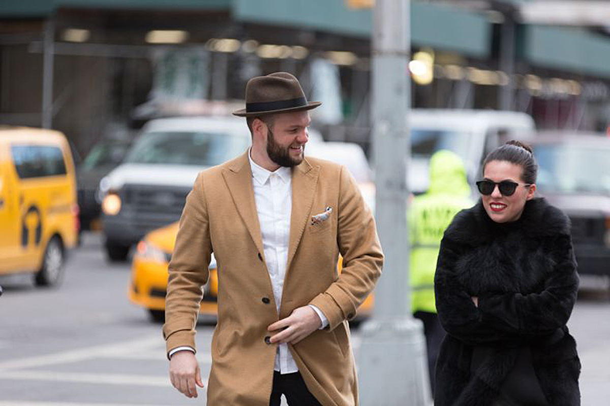 The MANIORPEDI founders — a man in a camel coat and hat walking with a woman in a black fur coat on a NYC street with yellow taxis