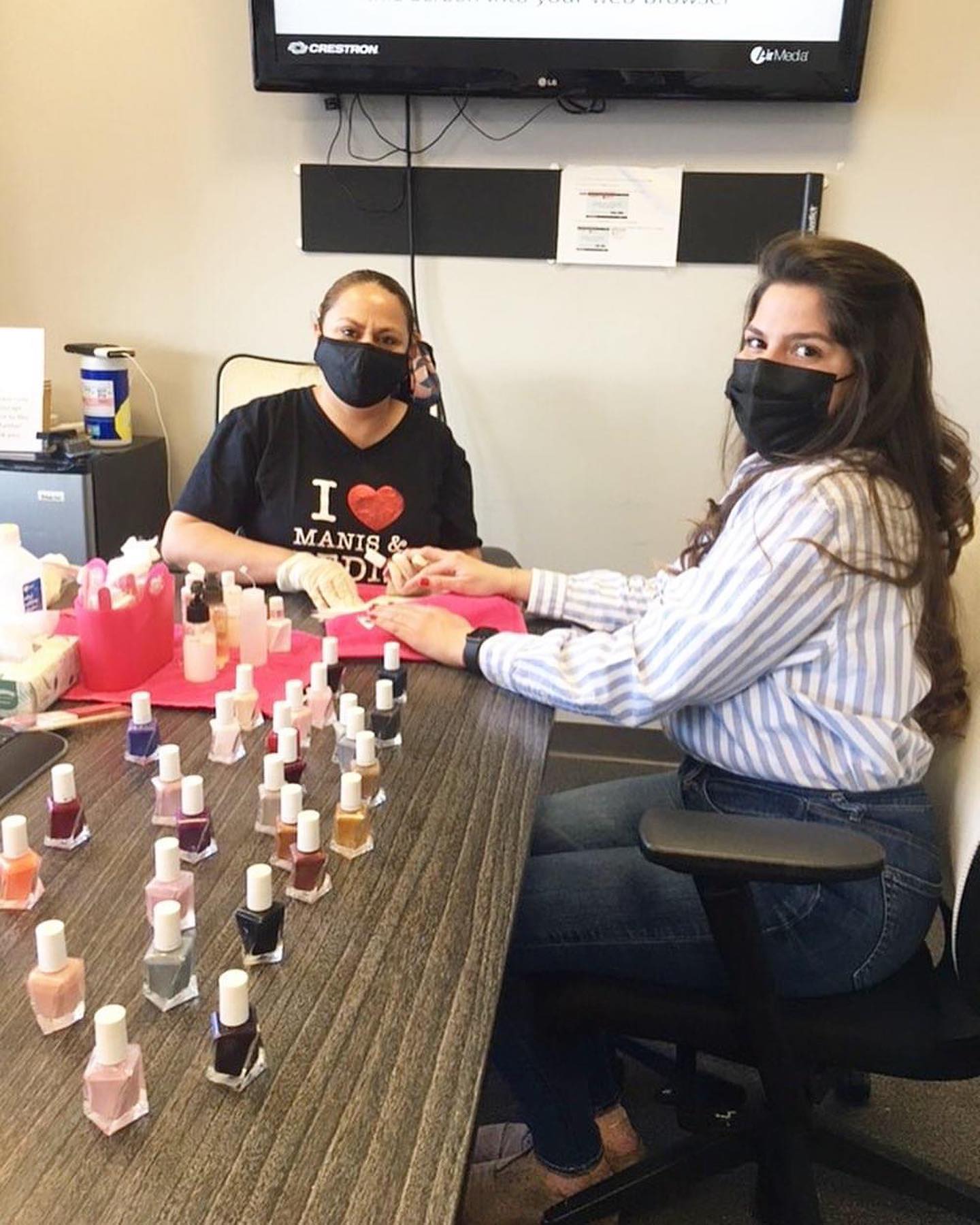 Nail technician in an I Love Manis and Pedis shirt doing a manicure at a conference table