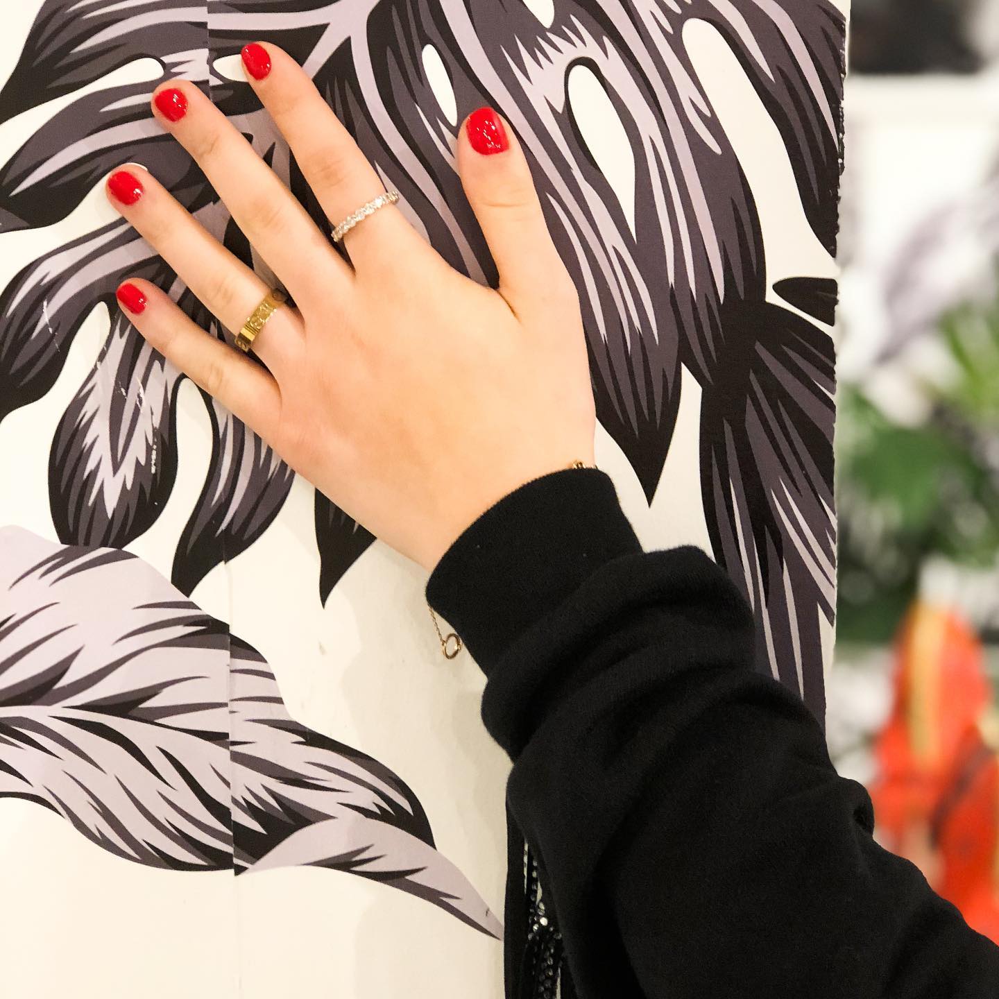 Hand with red nail polish against a black-and-white tropical leaf print background
